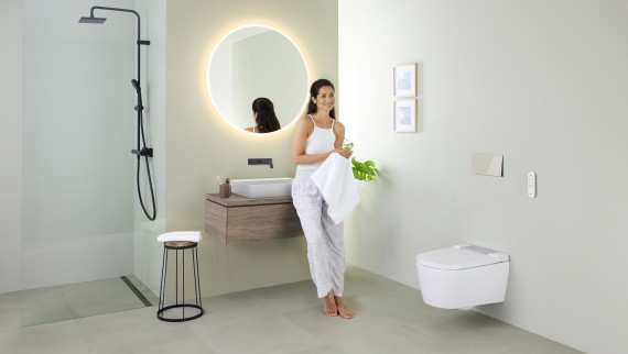 Geberit AquaClean Sela dušš-WC ja Geberit VariForm valamu ning mööbliga vannitoas valamule nõjatuv naine Geberit AquaClean Sela dušš-WC ja Geberit VariForm valamu ning mööbliga vannitoas valamule nõjatuv naine
